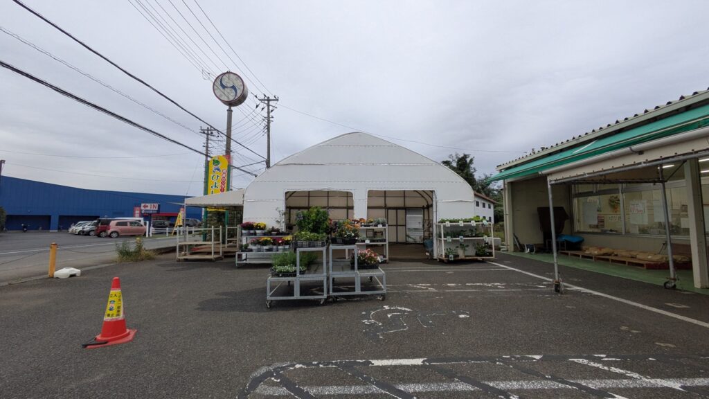 産直センター2号店の外観、花が並んだ棚と看板が見える駐車場の様子