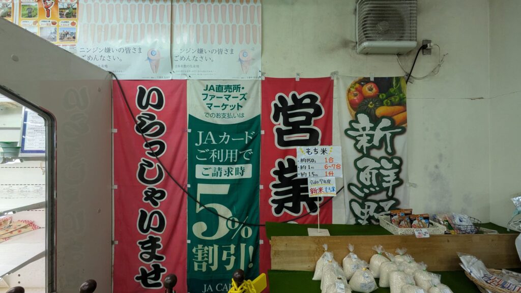 JA農業協同組合の産直センターの店内、営業案内の看板と新鮮野菜のイラストが見える。