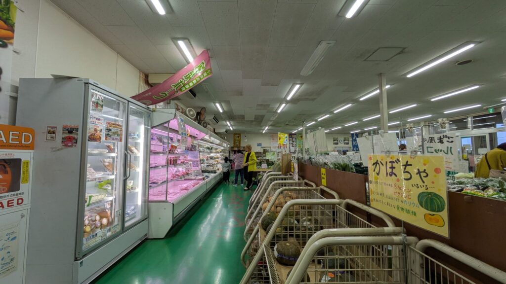 産直センターの内部写真。ピンクの冷蔵ケースと緑の床が特徴的で、新鮮な野菜や果物が並んでいる。