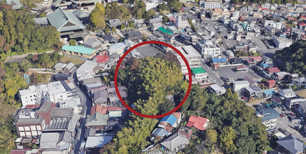 町の上空からの景色。緑の樹木が集まったエリアが赤い円で囲まれている。周囲には様々な建物や道路が広がっている。