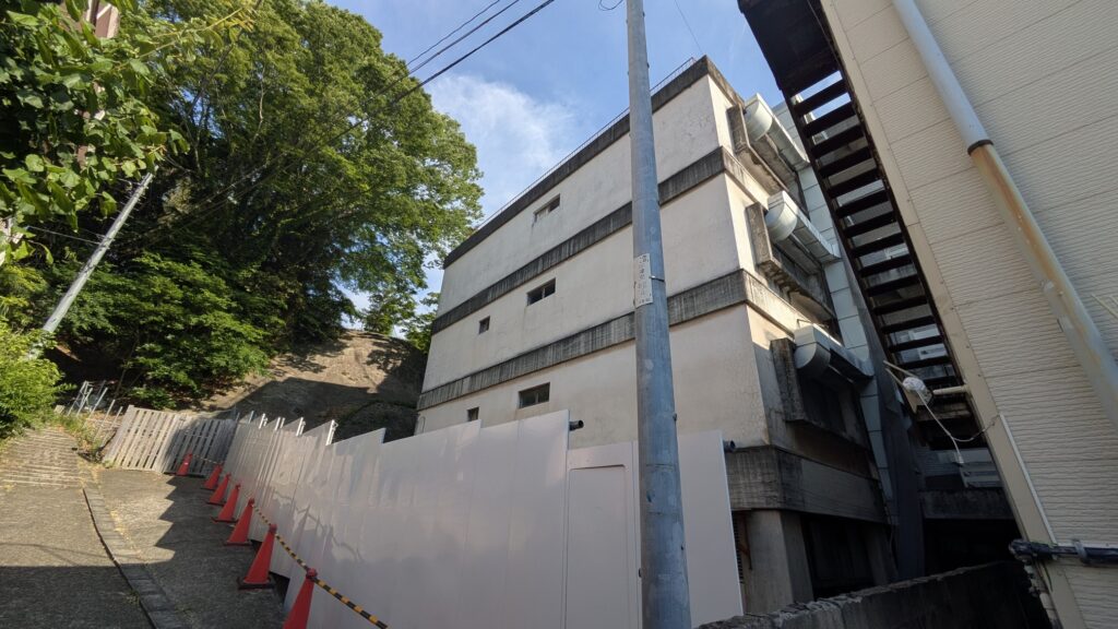 狭い路地沿いに立つ建物とその周囲の緑を見上げた風景