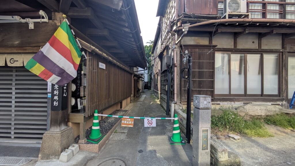 狭い路地に立つ木造の建物と、虹色の旗が掲げられた入口の風景