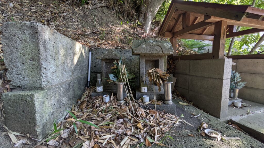 草むらに囲まれた石の墓地で、祭壇には植木や供え物が置かれている