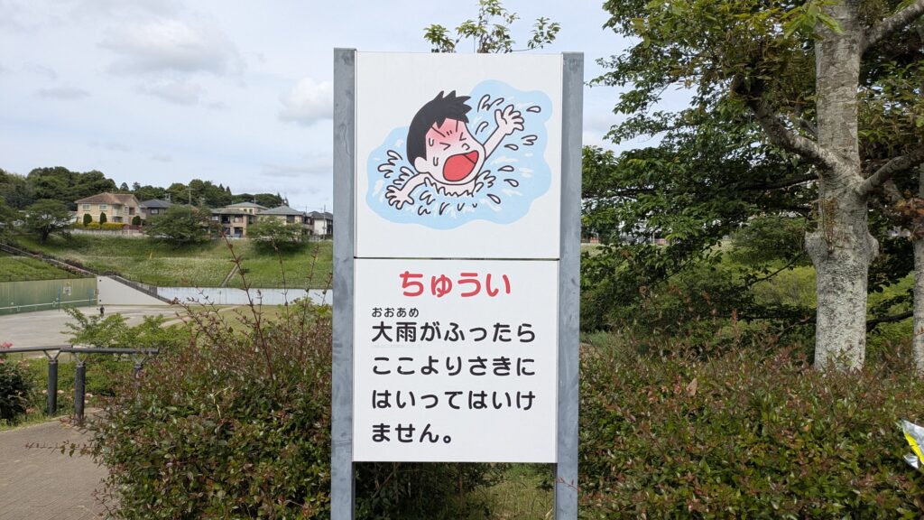 大雨時に入ってはいけない場所を警告する看板。イラストとして水に溺れる少年が描かれている。