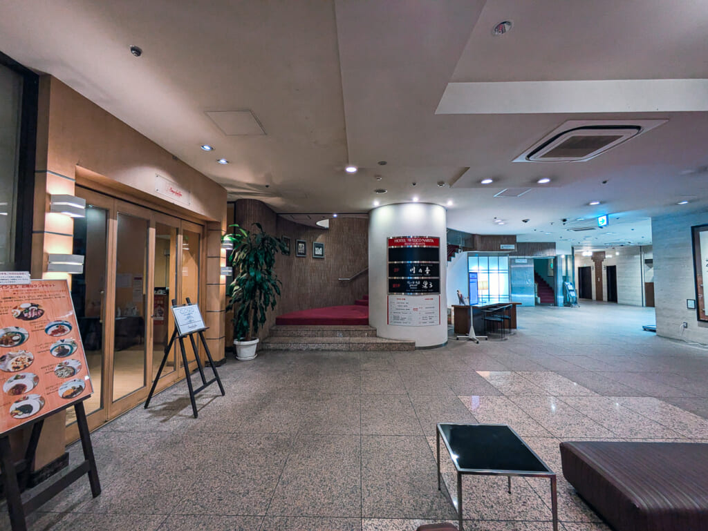 2026年10月撮影・成田市花崎町のホテルウェルコ成田 ロビー奥の赤い階段とレストランの看板|営業中