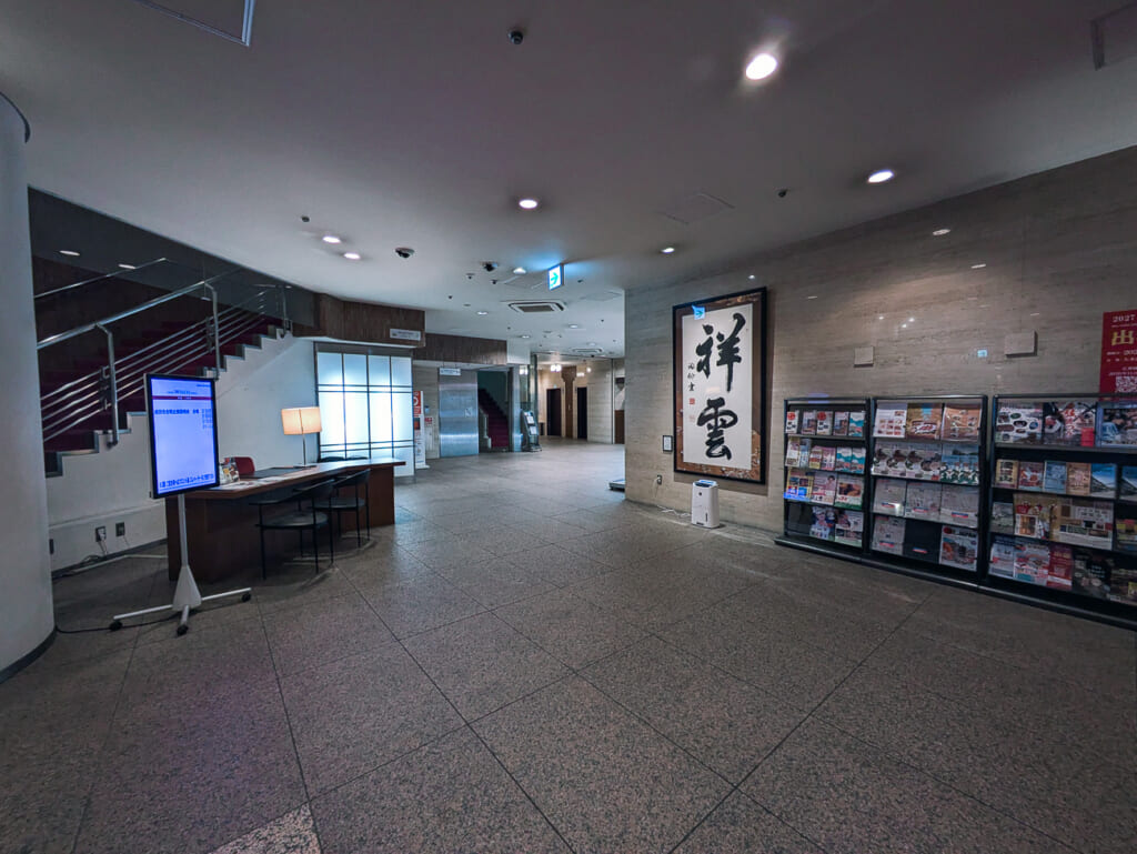 2026年10月撮影・成田市花崎町のホテルウェルコ成田 ロビーとフロント 書「祥雲」とパンフレットの棚|営業中