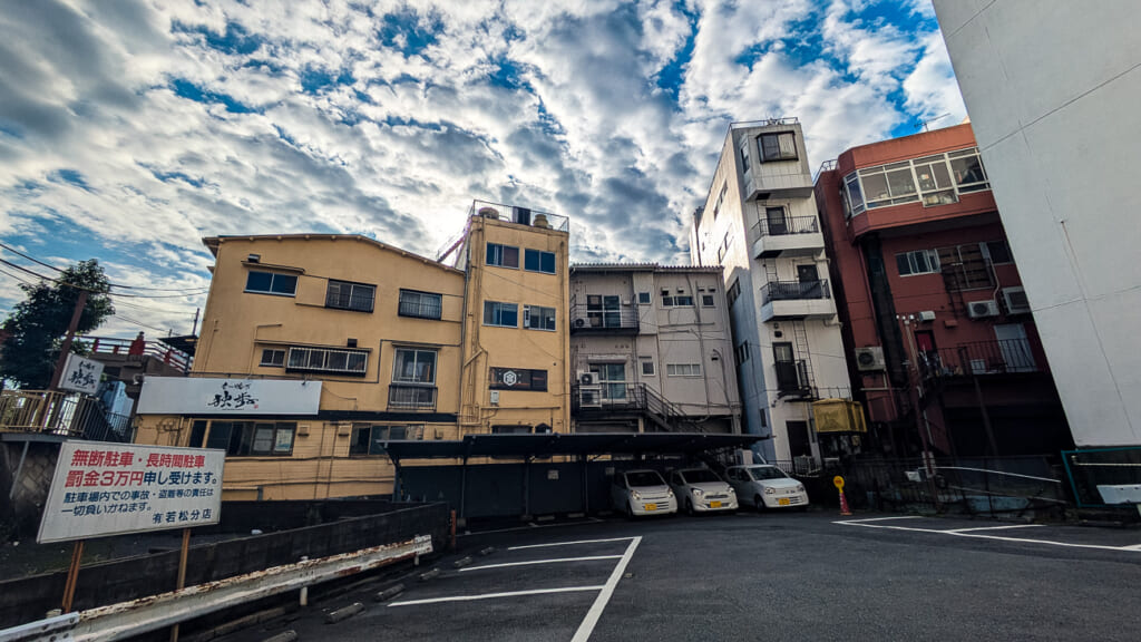 2026年撮影・成田市花崎町 千葉交通京成成田駅前ビル裏の駐車場と周りの建物｜現存