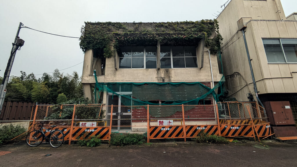 2026年10月撮影・成田市花崎町の開運ビル北隣 ツタに覆われた旧寄宿舎(1968年築)とフェンス|不明