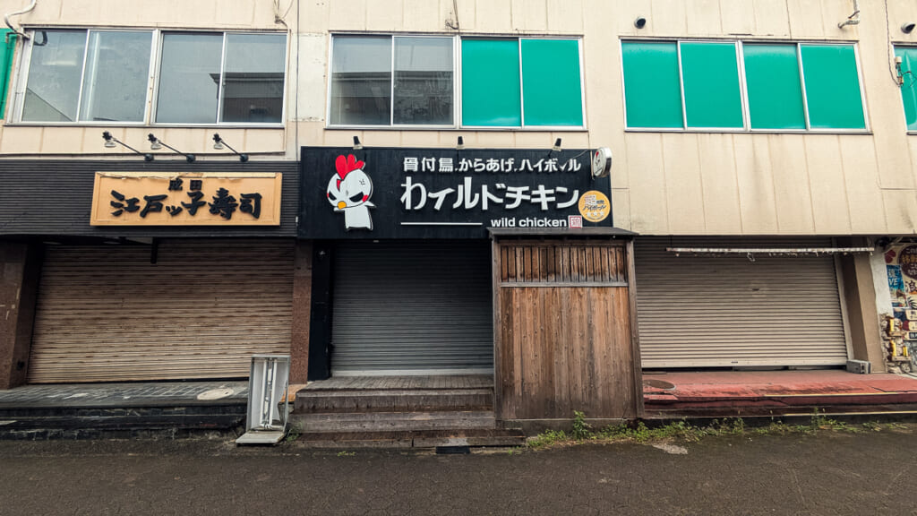2026年10月撮影・成田市花崎町の開運ビル ワイルドチキンの看板と木の扉|不明